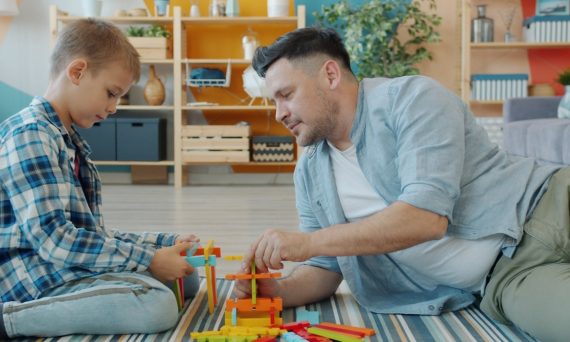Happy family father and child are playing with bright toys at home sitting on floor together using construction blocks. Childhood, playthings and house concept.